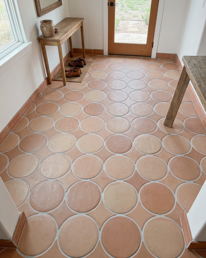 Terracotta round floor tiles arranged in a circular pattern inside a room with white walls, a wooden entryway console table, and a glass door.