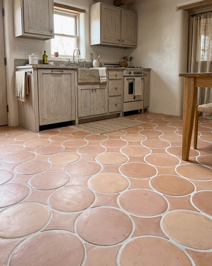 Terracotta oval floor tiles with white grout lines in a rustic kitchen setting with light wood cabinets and a vintage stove.