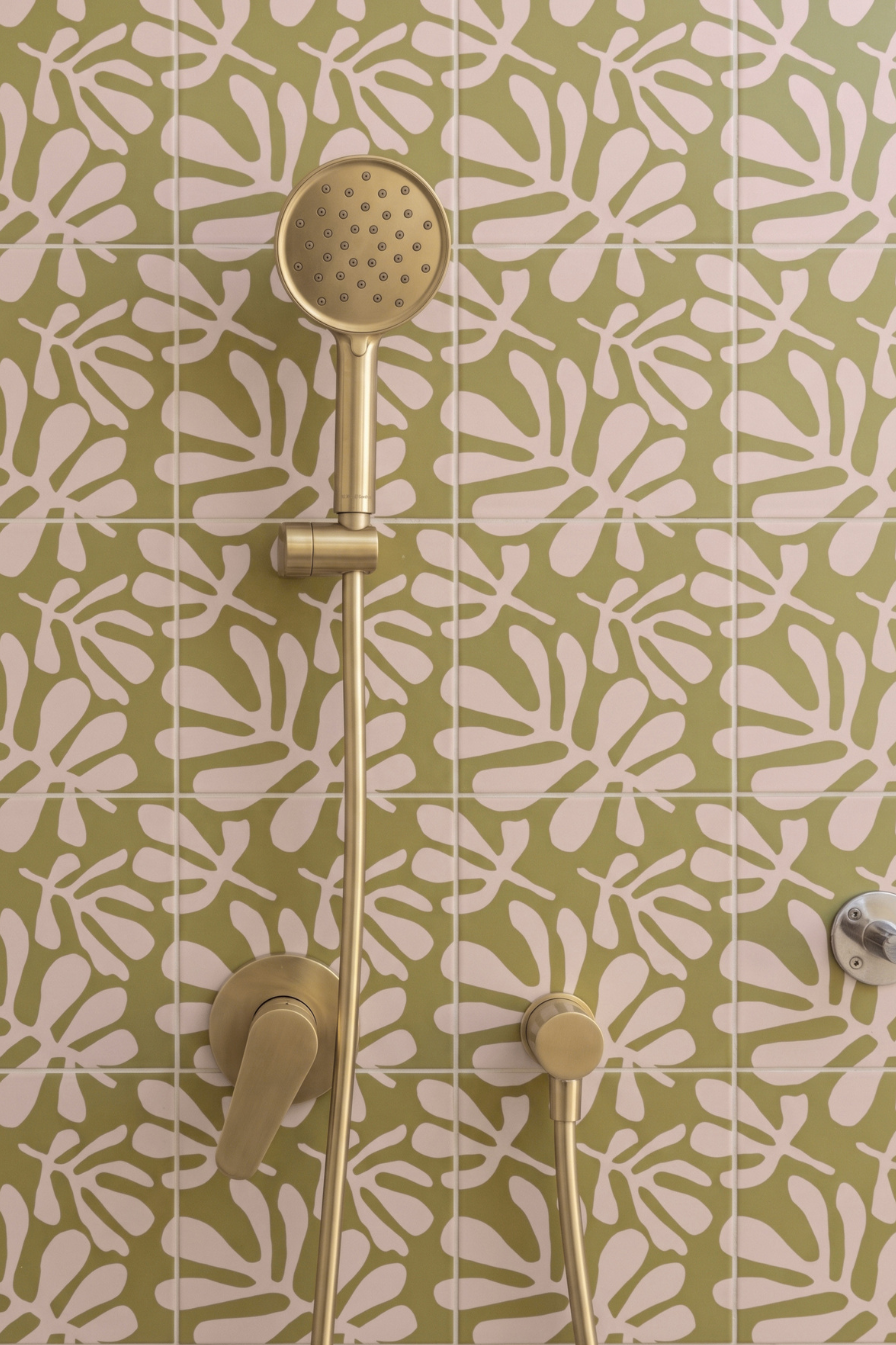 Gold shower fixture with a round hand shower head and matching controls mounted against a green and white patterned tile wall.