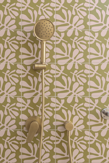 Gold shower fixture with a round hand shower head and matching controls mounted against a green and white patterned tile wall.
