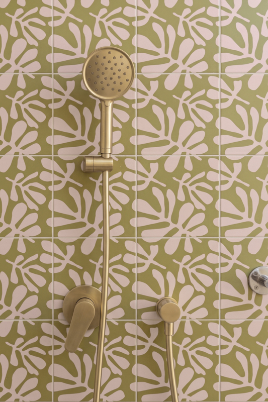 Gold shower fixture with a round hand shower head and matching controls mounted against a green and white patterned tile wall.