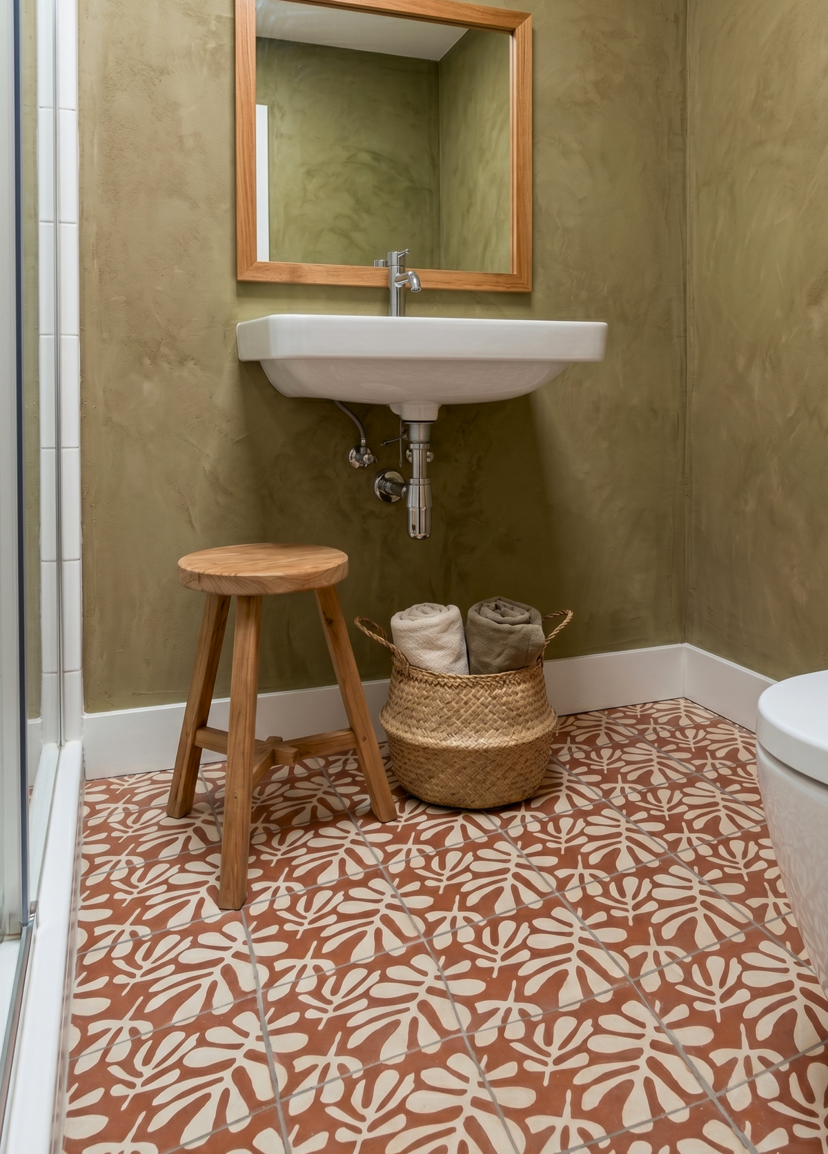 Bathroom with green walls, patterned red and white floor, wooden stool, and wicker basket.