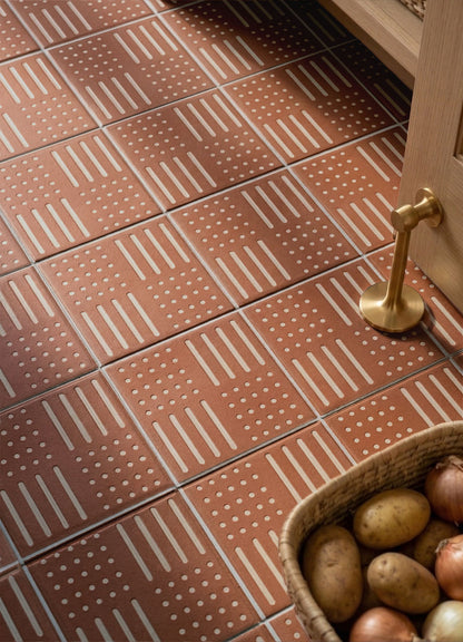 Terracotta pattern tile by Clay Imports featuring white dots and vertical lines in a staggered geometric design on a floor.
