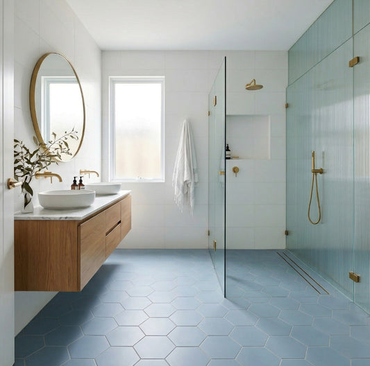 Blue hexagon clay tiles by Clay Imports covering a modern bathroom floor with a wooden vanity and glass shower enclosure.