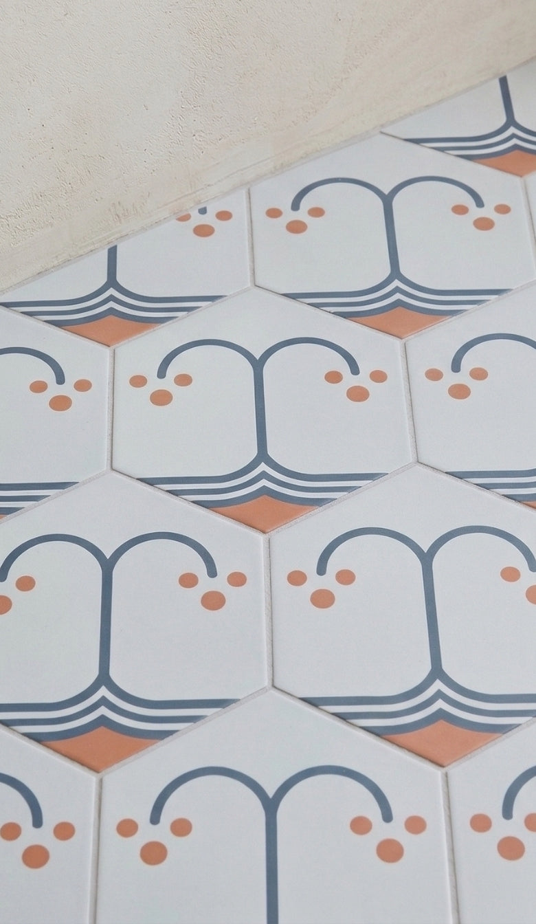 Hexagonal pattern tile by Clay Imports, white with blue-gray lines and orange dots, forming an abstract fruit-like design.