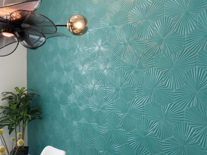 A modern geometric teal tile accent wall features dimensional, starburst-patterned hexagonal tiles illuminated by a stylish metallic light fixture.