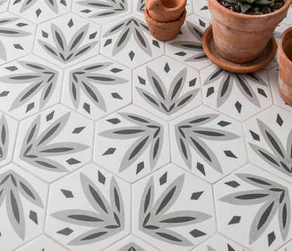 Hexagonal ceramic floor tiles with a repeating gray and charcoal botanical leaf pattern on a white background, styled with terracotta pots in the top right corner.