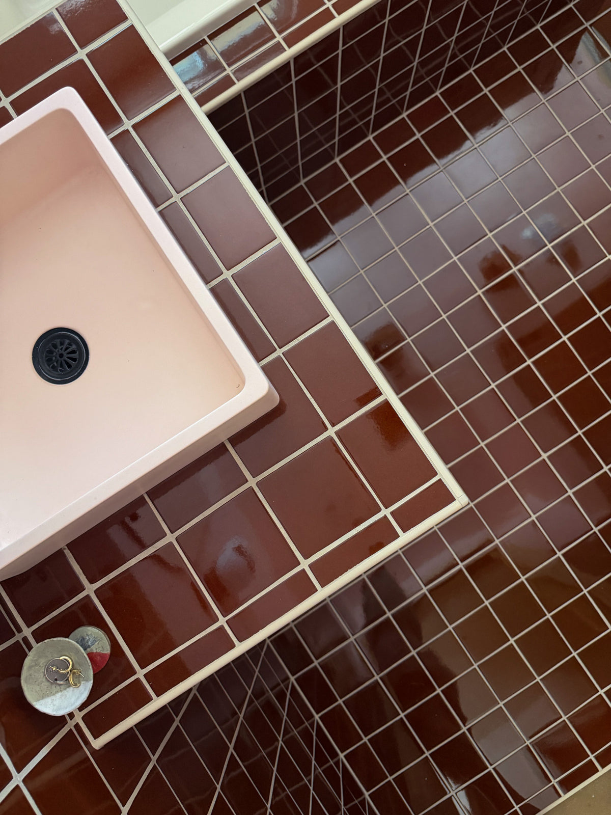 A pink rectangular sink with a black drain installed in a brown tiled bathroom counter.