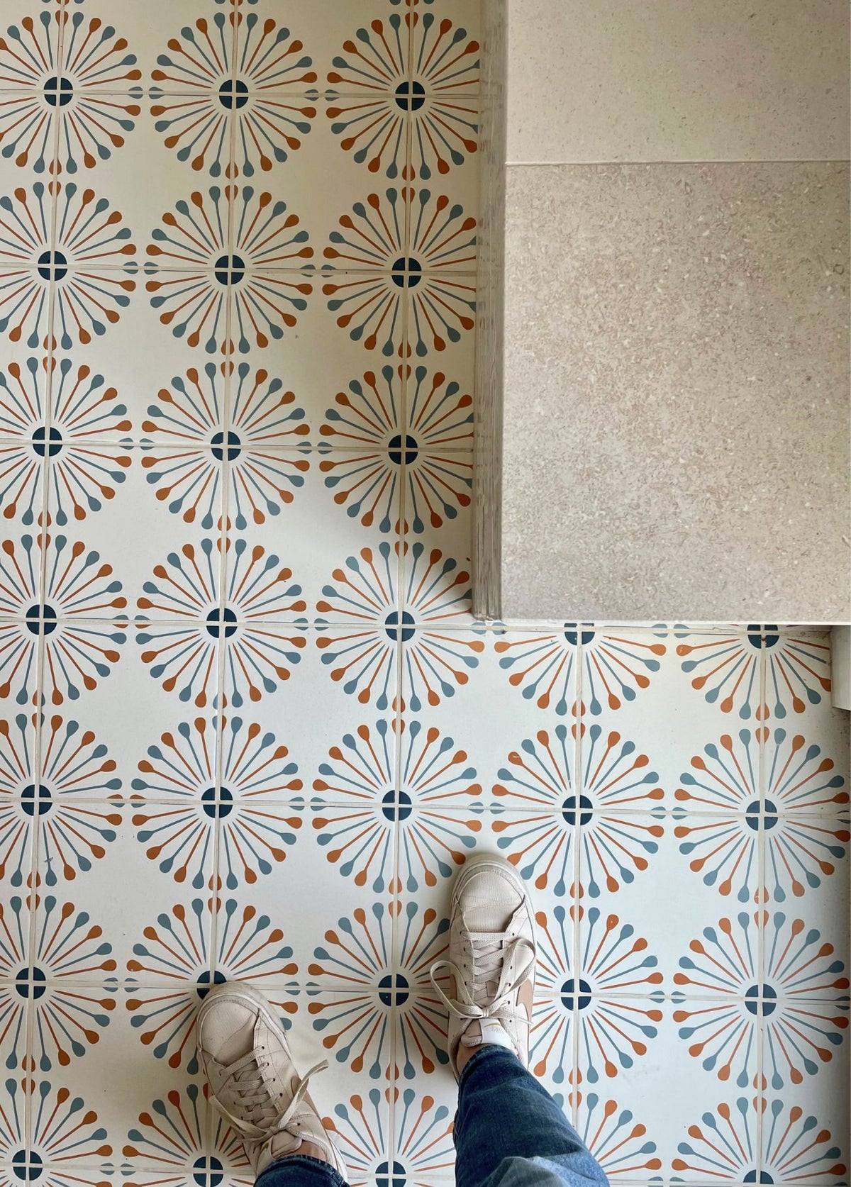 Atomic Vocho Papaya 8x8 Pattern Tile by Clay Imports, featuring blue and papaya-toned starburst designs on a cream background, with sneakers on the floor.