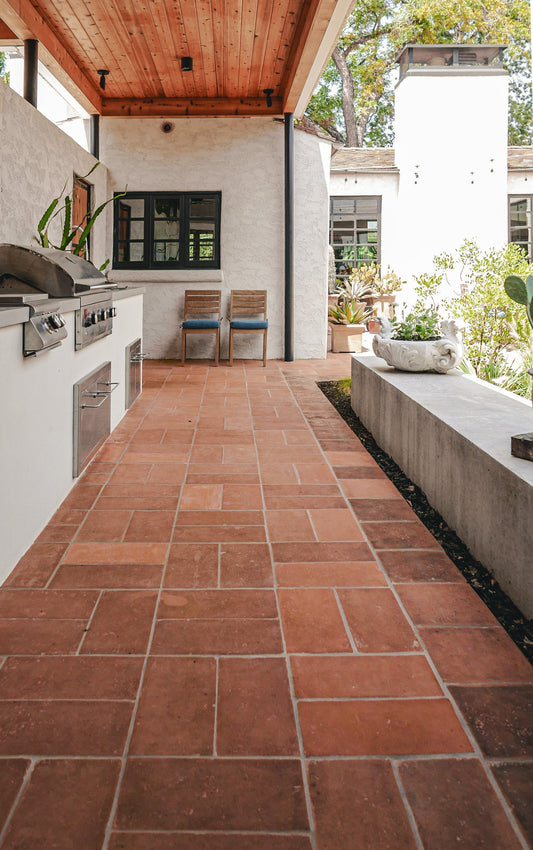 Terracotta clay tile pavers laid out in a rectangular pattern on an outdoor patio walkway, flanked by a white outdoor kitchen island on the left and a concrete planter bed on the right.