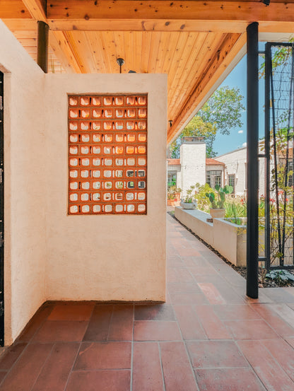 A warm-toned outdoor patio walkway with terracotta tile flooring, a stucco wall featuring a grid of glass blocks, and a wooden ceiling overhead.
