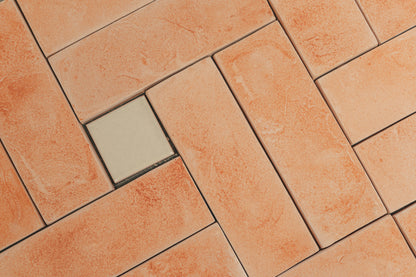 Terracotta-colored rectangular floor tiles arranged in a herringbone pattern, with one contrasting light beige square tile in the center.