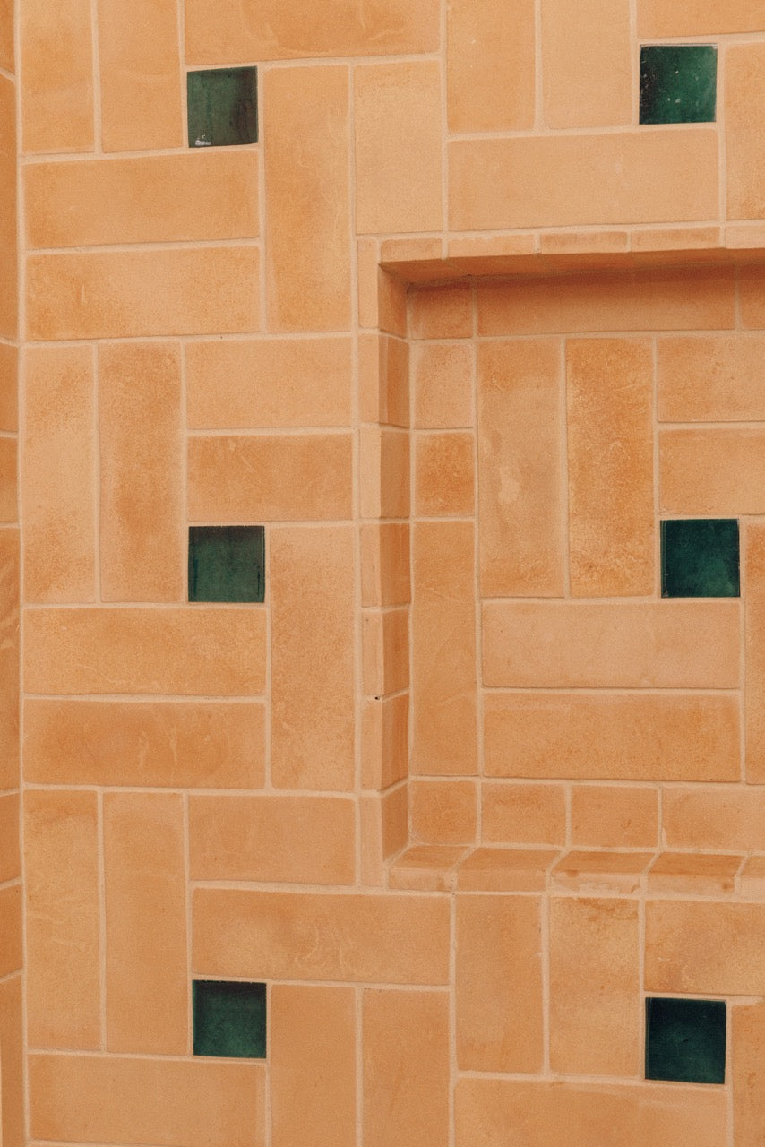 Terracotta orange stone tiles arranged in a geometric pattern with small dark green square accents.