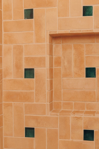 Terracotta orange stone tiles arranged in a geometric pattern with small dark green square accents.