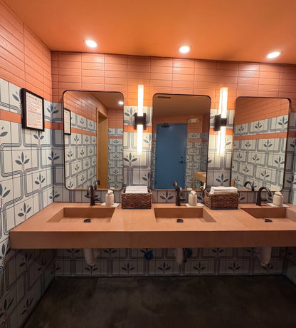 A modern three-sink bathroom vanity with a long wooden countertop, rectangular mirrors, patterned blue and white tiles, and warm orange walls and ceiling.