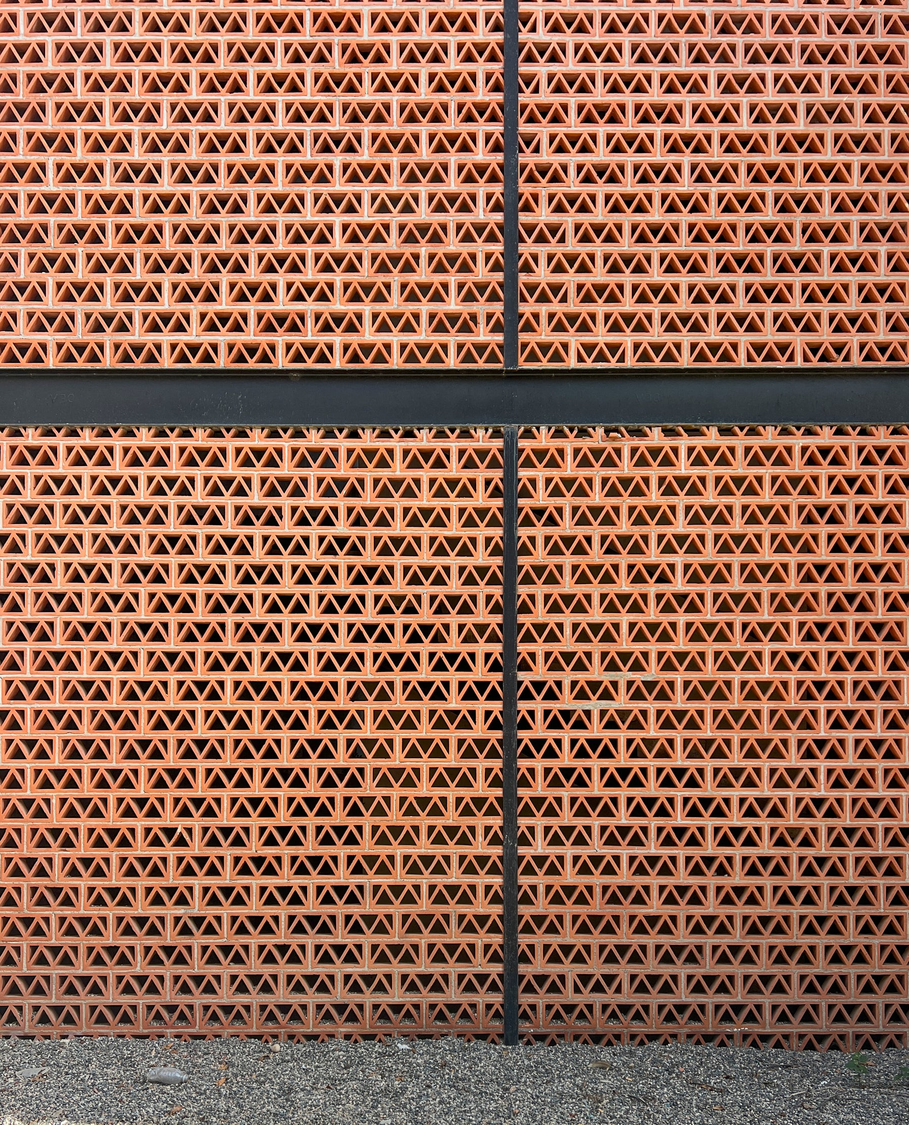 Terracotta breeze block with triangle pattern by Clay Imports, forming a wall with black beams and gravel.