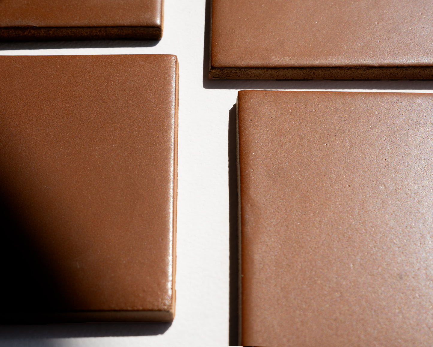 Rich brown square solid tile with matte textured surface, arranged in overlapping layout on white background, showcasing natural speckled finish and clean edges.