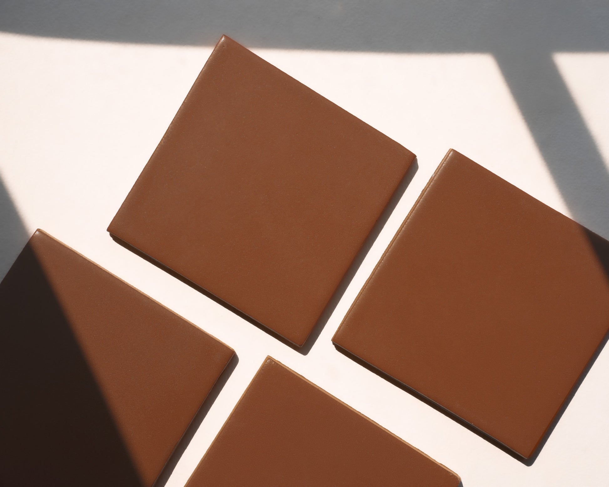 Rich brown square solid tile with smooth matte finish, arranged in diagonal pattern on white surface with natural shadow accents