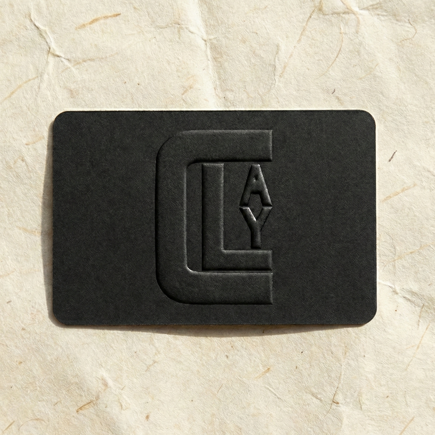 Black gift card by Clay Imports with an embossed 'CLAY' logo, placed on textured cream paper.