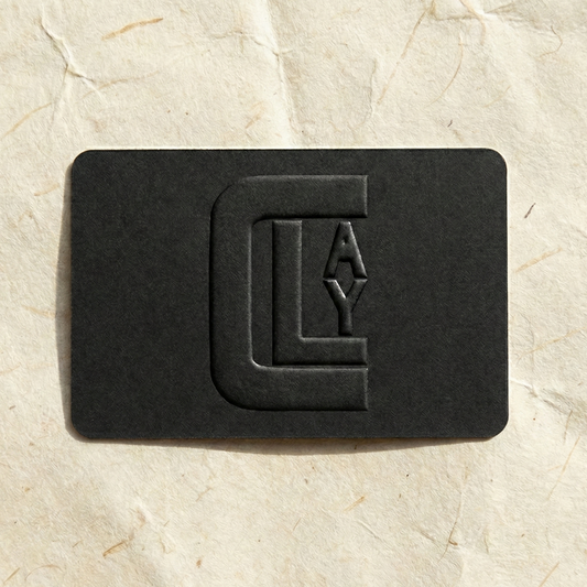 Black gift card by Clay Imports with an embossed 'CLAY' logo, placed on textured cream paper.