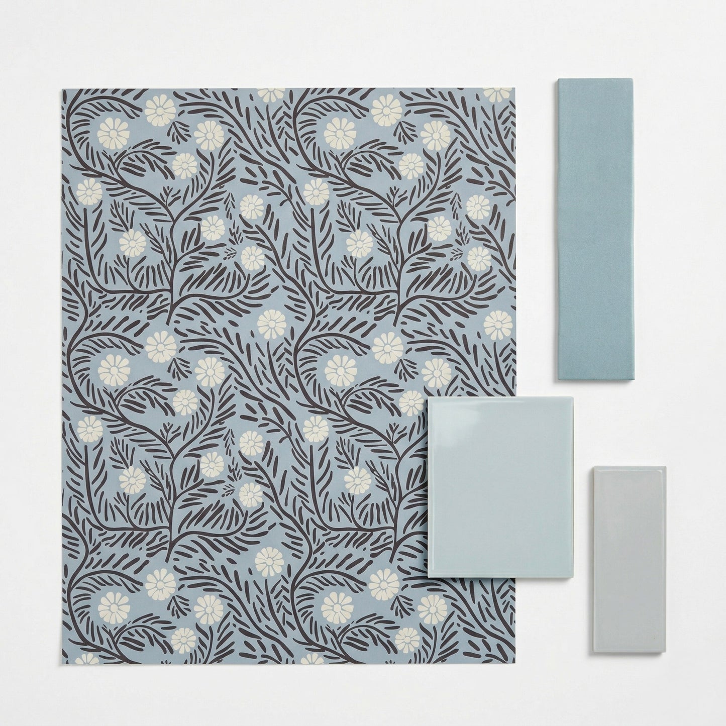 Light blue patterned tile by Clay Imports, featuring dark brown floral motifs and white daisy-like flowers, displayed with solid teal and light grey rectangular tiles.