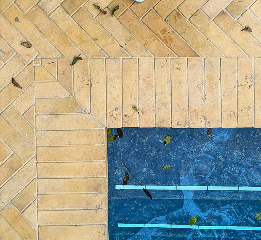 Light brown Cotto Dune tiles by Clay Imports in herringbone and straight patterns beside a blue pool with leaves.