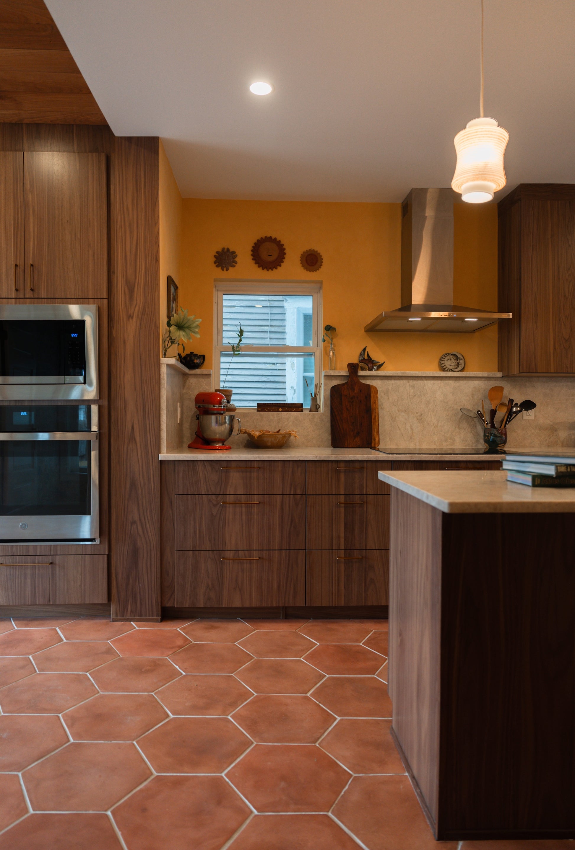 Modern kitchen with cotto terracotta floors, wooden cabinets, stainless steel appliances, and a yellow wall.