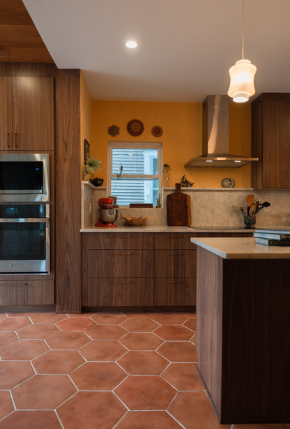 Modern kitchen with cotto terracotta floors, wooden cabinets, stainless steel appliances, and a yellow wall.