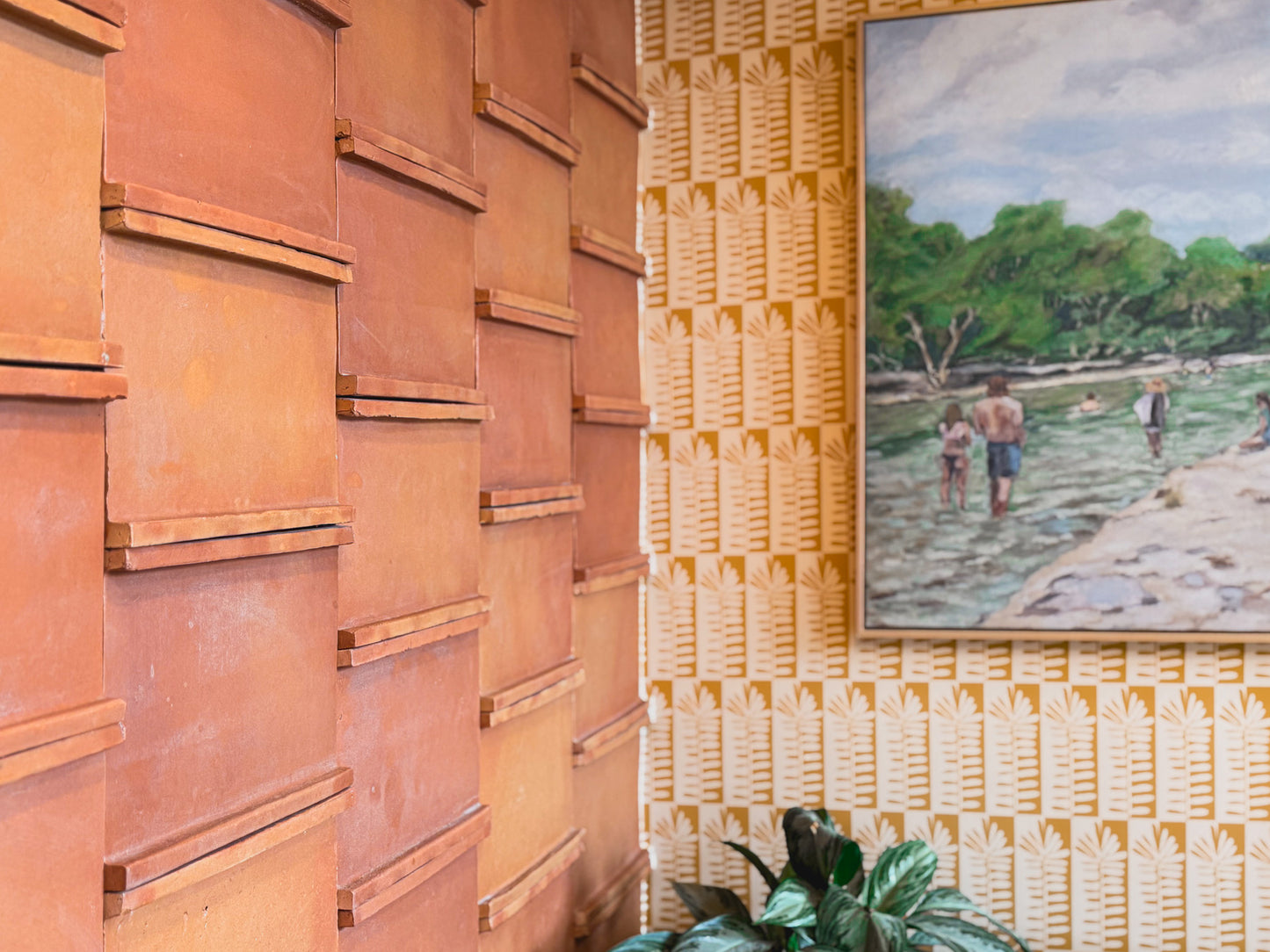 Textured terracotta Knotch Antique Satin tile by Clay Imports, with patterned wallpaper, a painting, and a plant nearby.