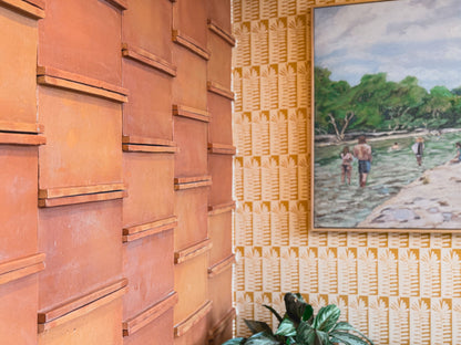 Textured terracotta Knotch Antique Satin tile by Clay Imports, with patterned wallpaper, a painting, and a plant nearby.