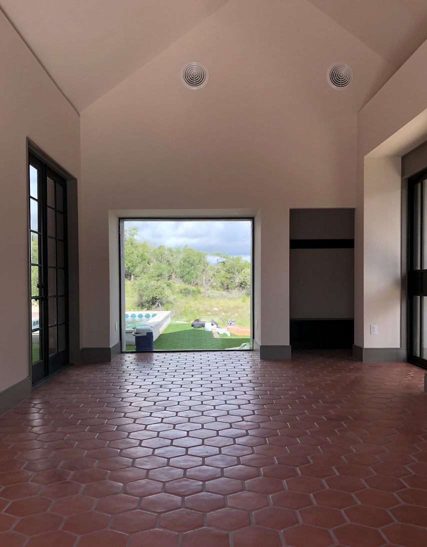 A modern sunroom features terracotta hexagonal floor tiles and a large central window framing a view of a lush outdoor landscape.