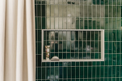 Emerald green subway tiled shower with a niche and ivory shower curtain