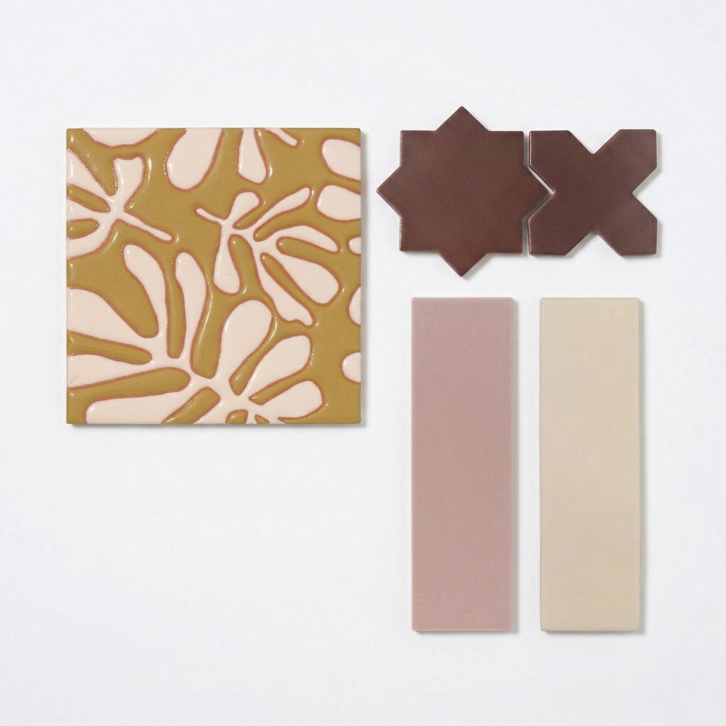 Assorted tile samples by Clay Imports, featuring an etched olive green organic pattern, brown star shapes, and solid pink and beige rectangular pieces.