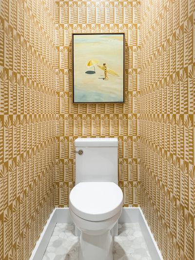 Small bathroom with patterned yellow floral wallpaper and marble floors and a framed picture above it.