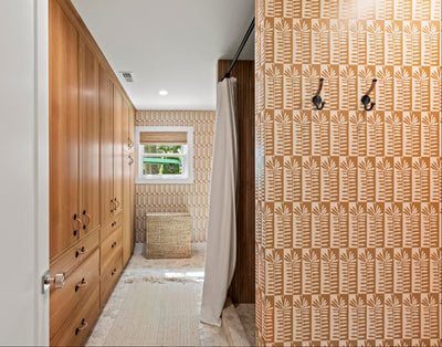 A narrow interior hallway with tall light wood cabinets on the left, a patterned orange-and-beige wall on the right, a white shower curtain, and a small window at the far end.