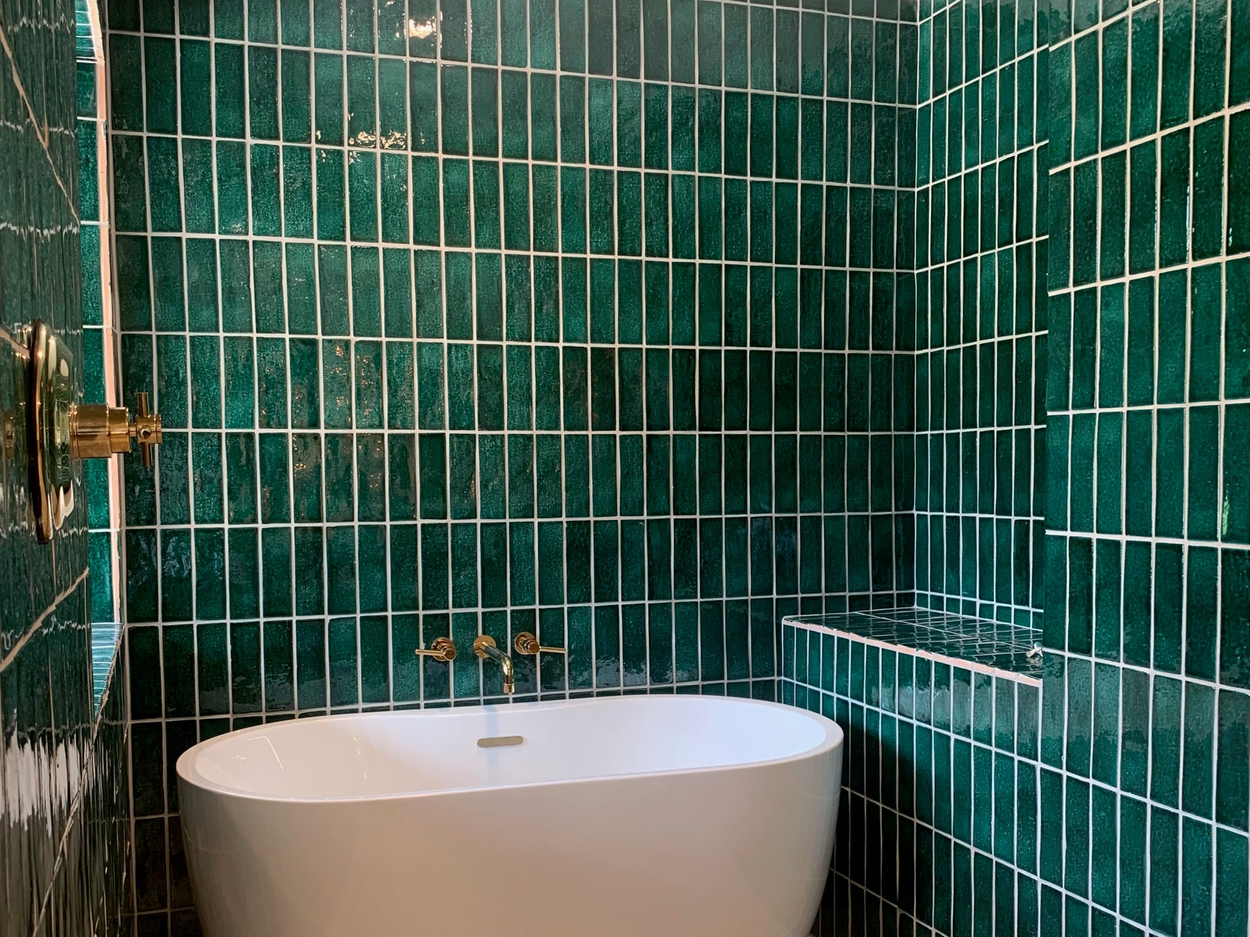 Forest green 2.5x8 glazed thin brick by Clay Imports, featuring variegated texture and white grout, installed vertically in a bathroom.