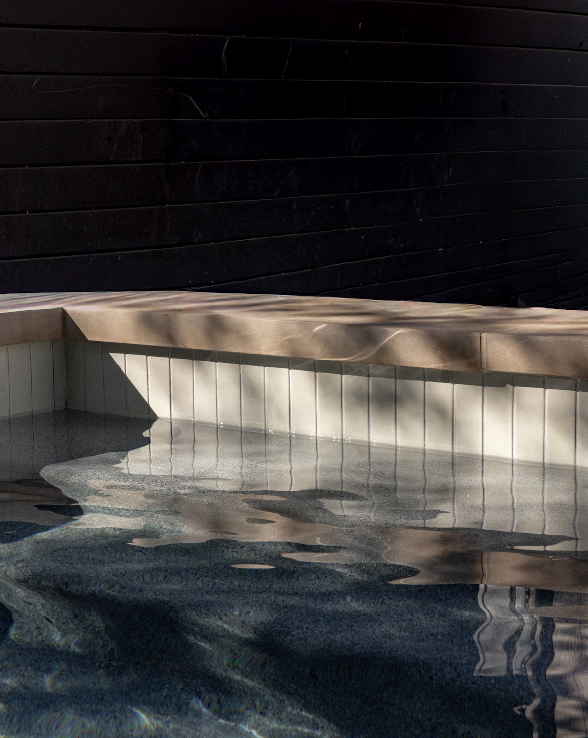Hailstone 2x6 Pool Waterline Tile by Clay Imports, light beige vertical tiles partially submerged in dark pool water.