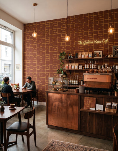 A cozy cafe interior with a wood-paneled counter, hanging pendant lights, and a copper espresso machine. Two people are seated at tables near a window on the left, and neon signage reads 'The Golden Hour Cafe'.