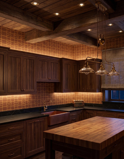 A rustic kitchen interior with dark wood cabinets, a wooden island, warm copper-toned tile backsplash, black countertops, and pendant lights under a wood ceiling.