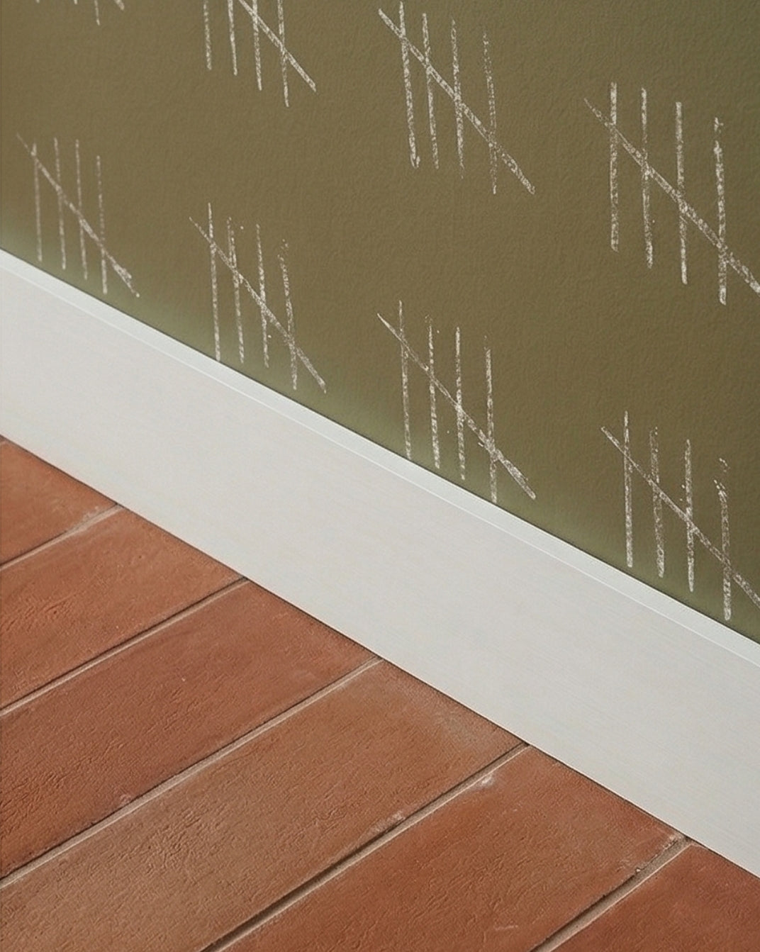 Umber Cotto floor tile from Clay Imports, with a textured finish, laid in planks against a green wall with white baseboard.