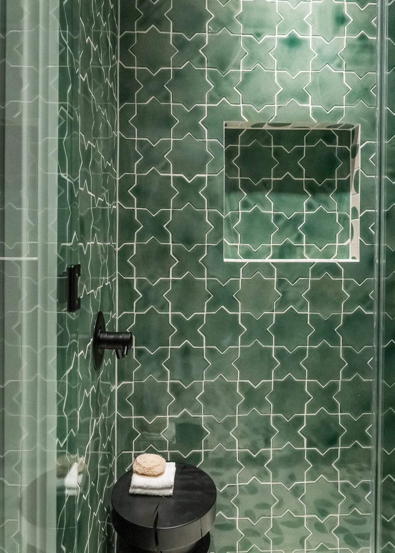 Varied green star and cross solid tile by Clay Imports, featuring white grout lines and a built-in shower niche.