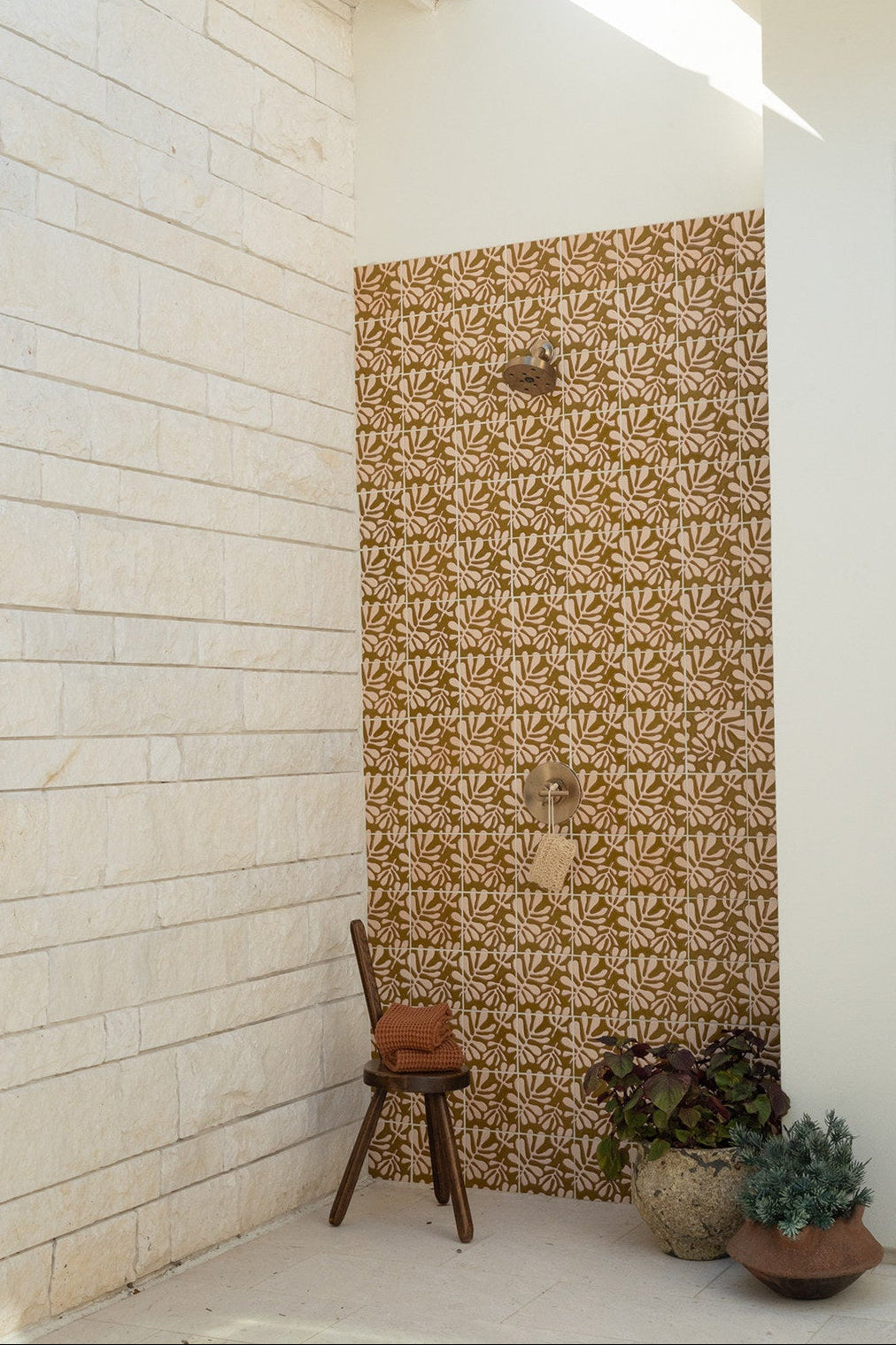 Decorative wall with jungle floral pattern tile in a sunlit outdoor shower area.