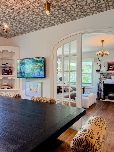 Living room with a large black dining table, patterned chairs, and a television on the wall.
