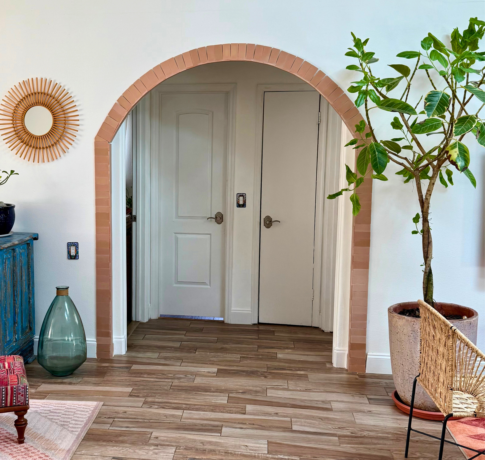 Archway leading to a room with wooden flooring, decorative elements, and a plant.