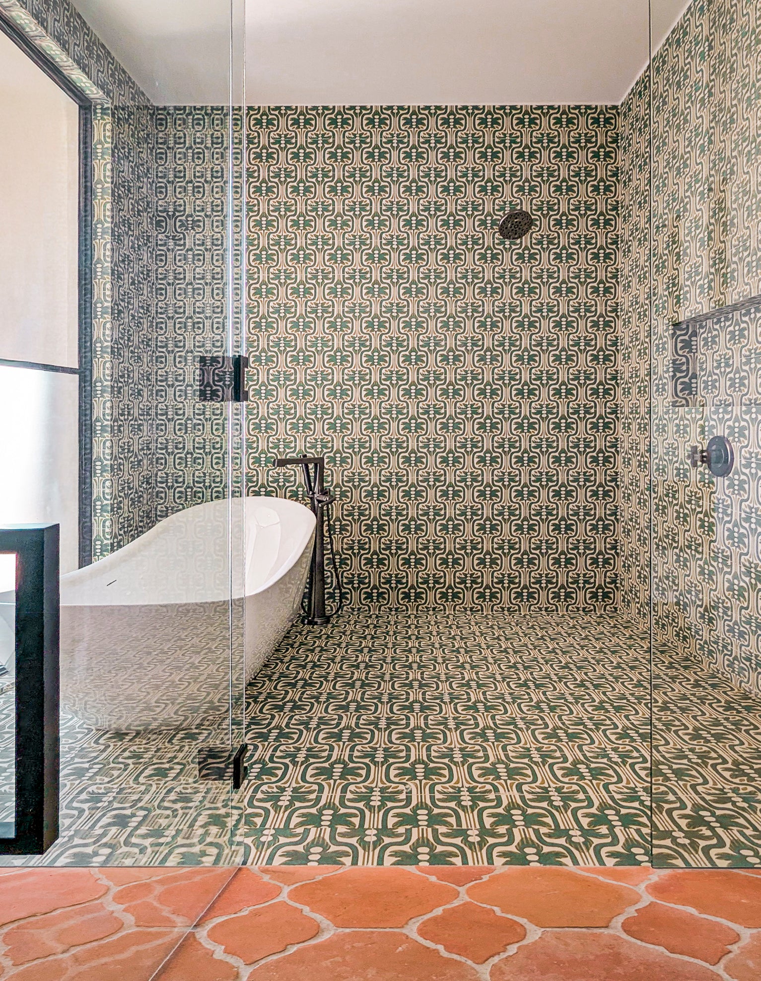 Green and beige pattern tile by Clay Imports, featuring an intricate repeating design covering a bathroom shower wall and floor.