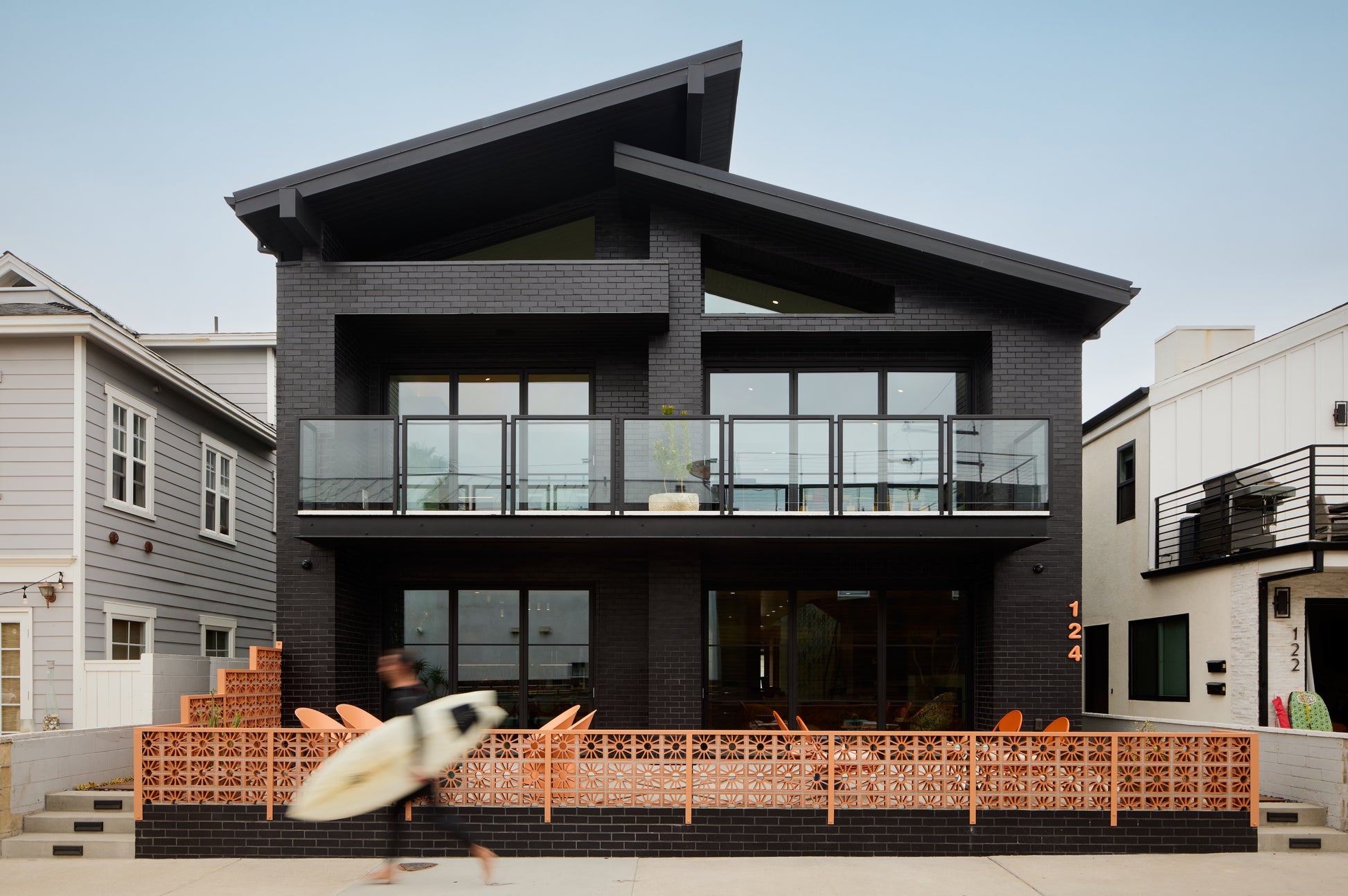 Modern black house with a breeze block fence and aperson holding a surfboard in front