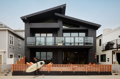 Modern black house with a breeze block fence and aperson holding a surfboard in front