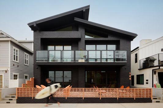 Modern black house with a breeze block fence and aperson holding a surfboard in front