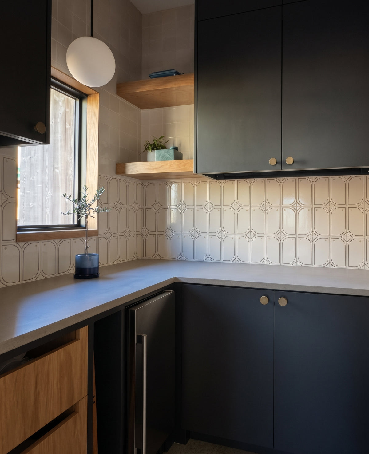 A modern kitchen features dark charcoal cabinets, light countertops, and unique patterned tile backsplash with open wooden shelves displaying decor.