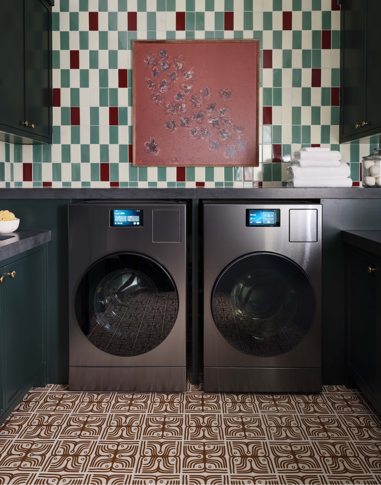 Pair of washing machines in a laundry room with decorative tiles and a painting on the wall.